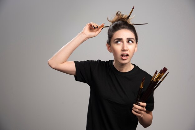 Belle femme avec chignon en désordre tenant des pinceaux.