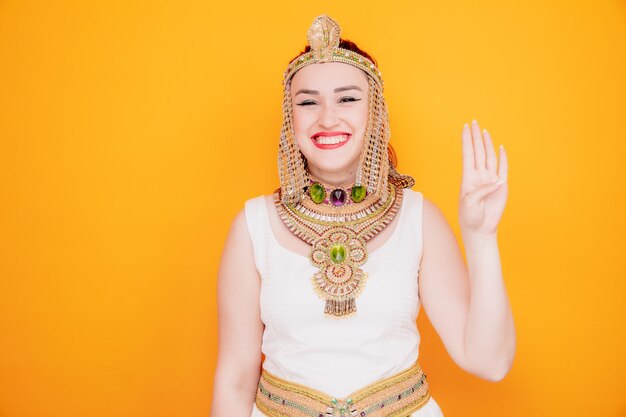 Belle femme comme Cléopâtre en costume égyptien antique souriant heureux et joyeux montrant le numéro quatre avec les doigts sur orange