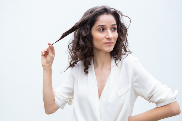 Belle femme confiante positive tenant une mèche de cheveux bouclés