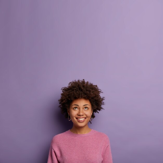 Belle femme curieuse à la peau sombre regarde avec intérêt et sourire au-dessus