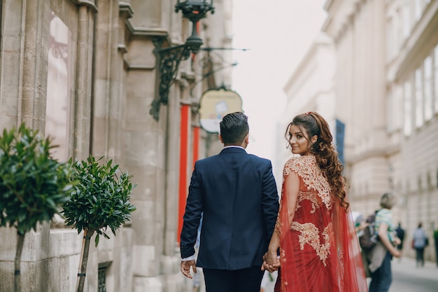 Belle femme dans une longue robe rouge se promène dans la ville avec son mari