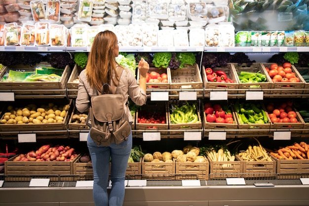 Belle femme debout devant des étagères de légumes en choisissant quoi acheter