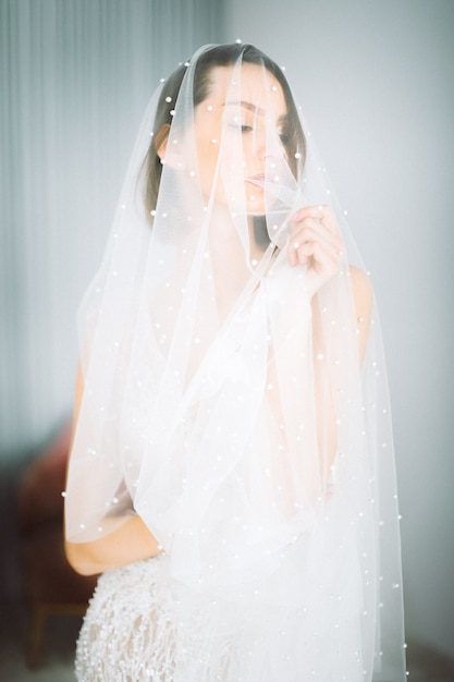 Belle femme debout et regardant en robe de mariée dans la chambre