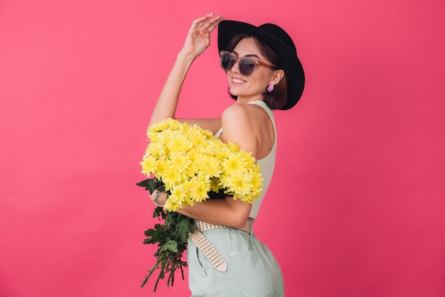 Belle femme élégante en chapeau et lunettes de soleil posant, tenant un grand bouquet d'asters jaunes, humeur printanière, espace isolé des émotions positives