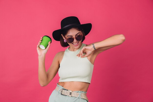 Belle femme élégante en chapeau et lunettes de soleil posant, tenant une tasse de papier de danse de café active en mouvement heureux émotions positives,