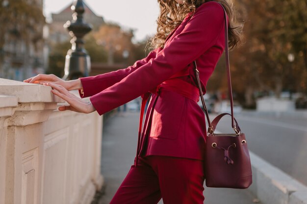Belle femme élégante en costume violet marchant dans la rue de la ville, tendance de mode printemps été saison automne portant chapeau, tenant sac à main