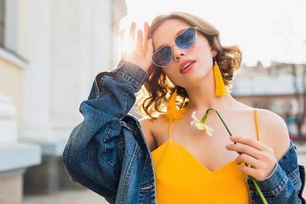 Belle femme élégante sexy en robe élégante jaune portant une veste en jean, tenue à la mode, tendance de la mode printemps-été, ensoleillé, lunettes de soleil bleues, mode de rue, style hipster, accessoires à la mode