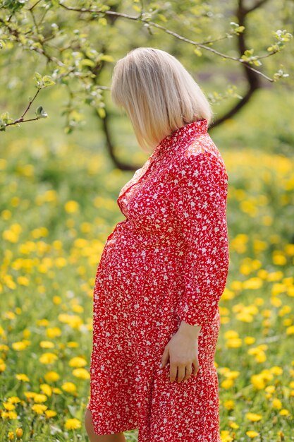 Belle femme enceinte se détendre dans le parc vêtue d'une robe rouge