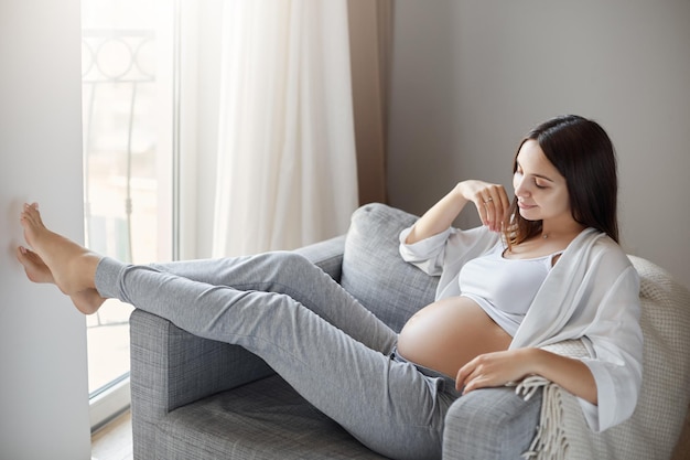 Belle femme enceinte se détendre à la maison rêvant de voyager et de mettre son corps en forme Parlant silencieusement à son bébé Concept de grossesse