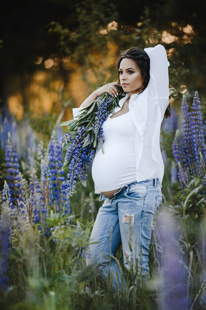 Belle femme enceinte se tient avec un bouquet de lupin parmi la pelouse