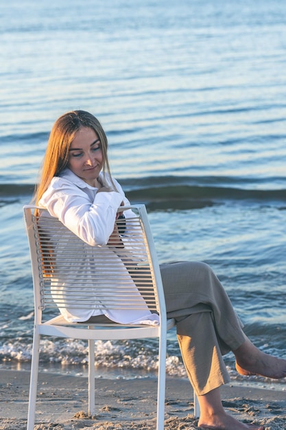 Une belle femme est assise sur une chaise près de la mer