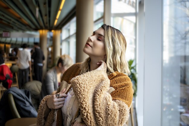 Belle femme européenne portant un manteau orange à la mode et profitant de son temps dans un café