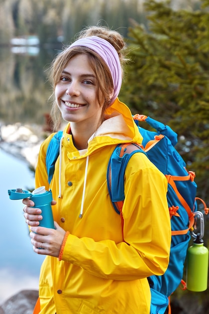 Belle femme avec une expression faciale heureuse, vêtue d'un imperméable jaune, porte un sac à dos