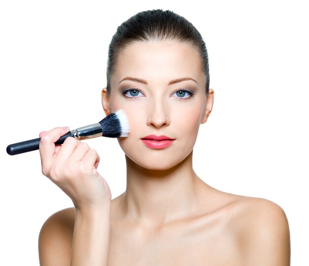 Belle femme faisant du maquillage sur le visage avec une brosse cosmétique isolé sur blanc