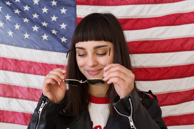 Belle femme féminine ou adolescente porte de nouvelles lunettes de soleil devant le drapeau américain, hipster à la mode et à la mode, patriote des États-Unis