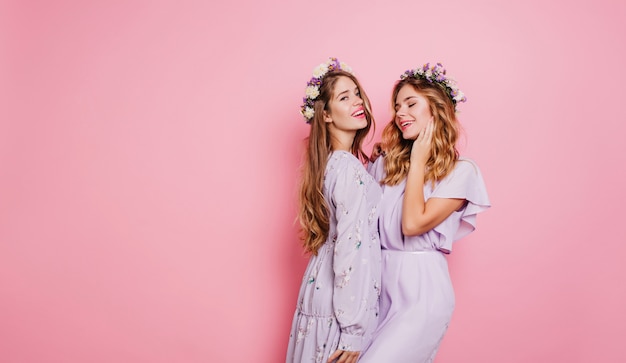 Belle femme en guirlande de fleurs souriant sur mur rose