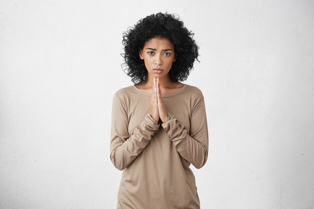 Belle femme habillée avec désinvolture gardant les paumes pressées l'une contre l'autre devant elle, ayant un regard regrettable et désolé, implorant pardon. Expressions faciales humaines, émotions et langage corporel