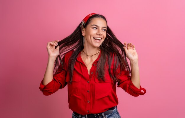 Belle femme hispanique en chemise rouge posant souriant sur rose isolé portant un bandeau