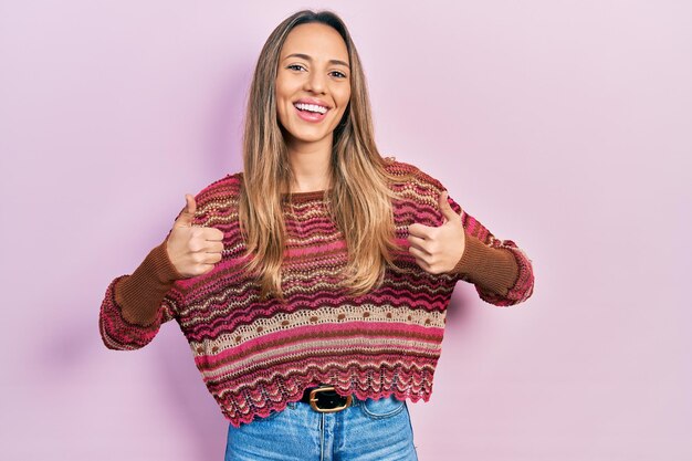 Belle femme hispanique portant un signe de succès pull hippie faisant un geste positif avec la main pouce levé souriant et heureux expression joyeuse et geste gagnant