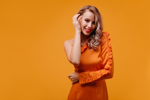 Belle femme avec jolie coiffure bouclée souriant sur mur jaune