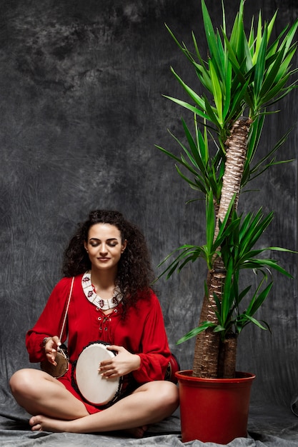 Photo gratuite belle femme jouant du tambour dans les plantes tropicales sur mur gris