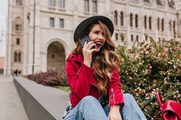 Belle femme avec une longue coiffure ondulée, parler au téléphone sur le mur de l'architecture