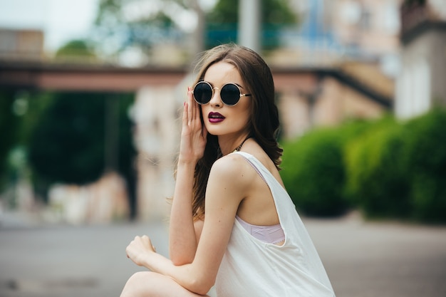 Belle femme à lunettes de soleil assise sur l'asphalte