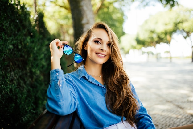 Belle femme à lunettes sourire reposant sur un banc dans le parc