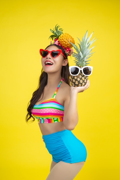 Belle femme en maillot de bain tenant un ananas pose sur jaune