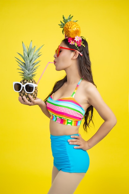 Belle femme en maillot de bain tenant un ananas pose sur jaune