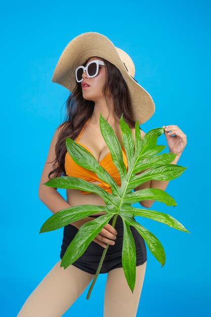 Une belle femme en maillot de bain tenant une feuille verte pose sur bleu