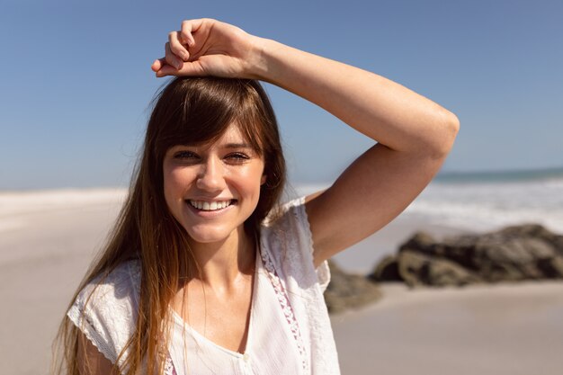 Belle femme avec la main sur la tête en regardant la caméra sur la plage au soleil