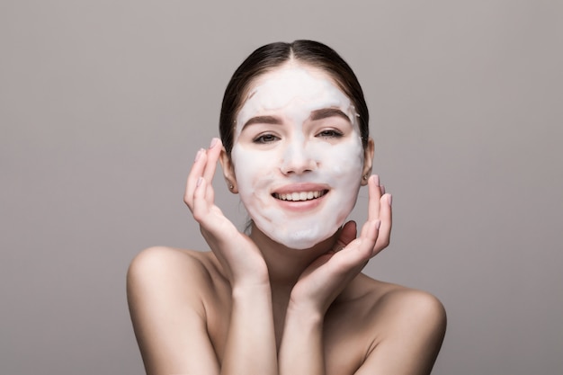 Belle femme avec masque facial sur mur blanc. Cosmétiques, soins de la peau.