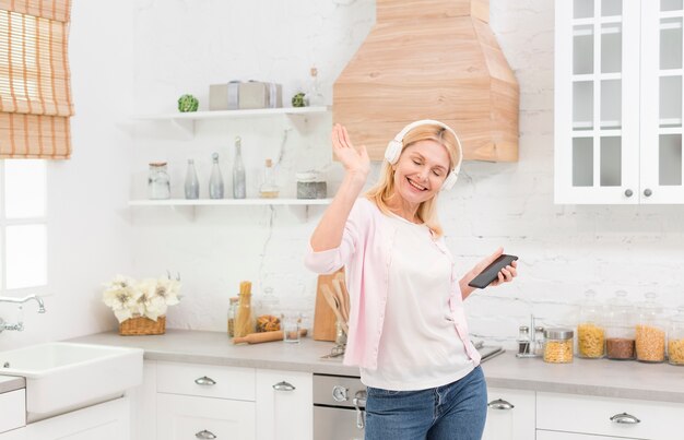 Belle femme mature, écouter de la musique dans la cuisine