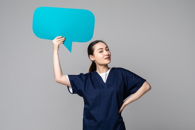 Belle femme médecin asiatique isolée sur un mur blanc et tenant du papier bulle vierge le symbole de parler de quelque chose d'important