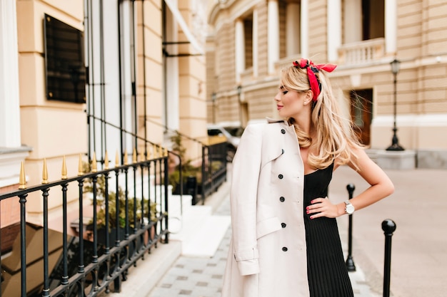 Belle femme mince en robe noire posant avec plaisir sur la vieille rue étroite