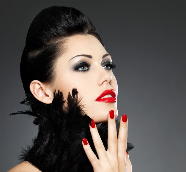 Belle femme de mode avec des ongles rouges, coiffure créative et maquillage