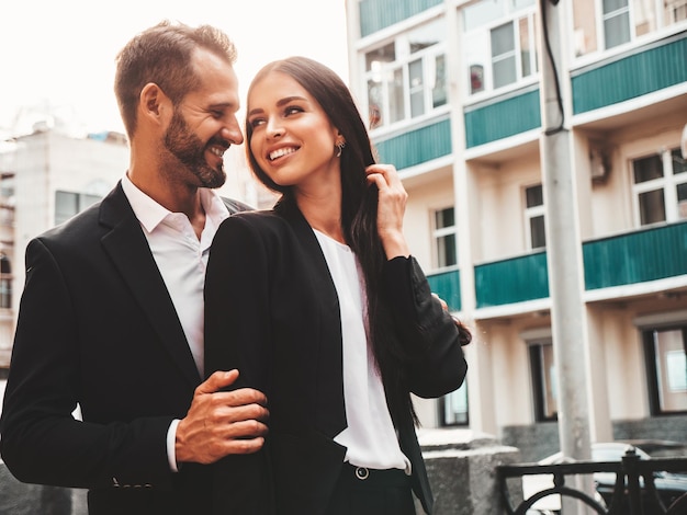 Photo gratuite belle femme de mode et son beau petit ami en costume sexy modèle brune souriante en robe de soirée noire couple à la mode posant dans la rue au coucher du soleil homme brutal et sa femme à l'extérieur