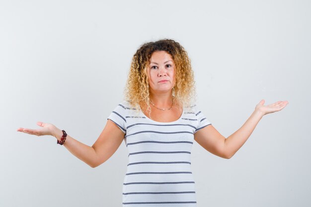 Belle femme montrant un geste impuissant en t-shirt et semblant hésitante, vue de face.