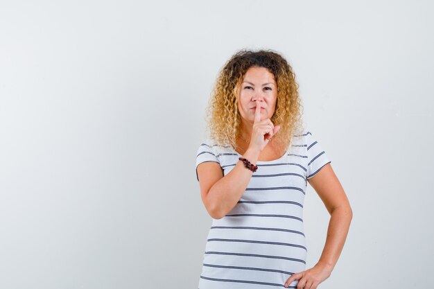 Belle femme montrant un geste de silence en t-shirt et l'air confiant. vue de face.