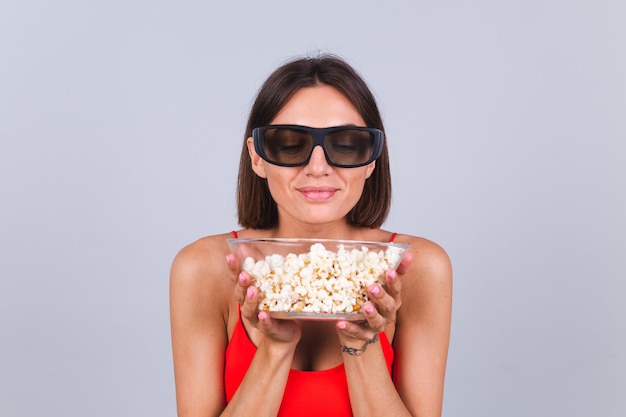 Belle femme sur mur gris dans des lunettes de cinéma 3d avec pop-corn, émotions positives joyeuses et heureuses