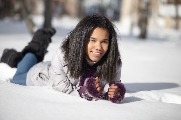Belle femme noire américaine souriante couchée dans la neige à l'extérieur