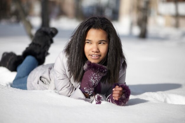 Belle femme noire américaine souriante couchée dans la neige à l'extérieur