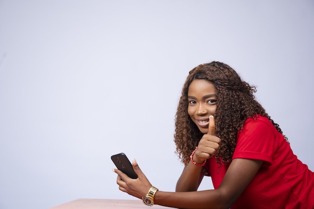 Belle femme noire assise sur le côté, tenant son téléphone et un coup de pouce