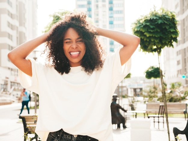 Photo gratuite belle femme noire avec des boucles afro coiffuremodèle hipster souriant en t-shirt blanc sexy femme insouciante posant sur le fond de la rue gai et heureux