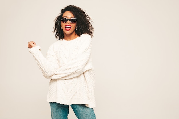 Belle femme noire avec une coiffure de boucles afro et des lèvres rouges. Modèle souriant dans des vêtements de jeans à la mode et un pull d'hiver.