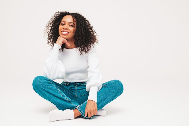 Belle femme noire avec une coiffure de boucles afro. Modèle souriant en pull et vêtements jeans à la mode