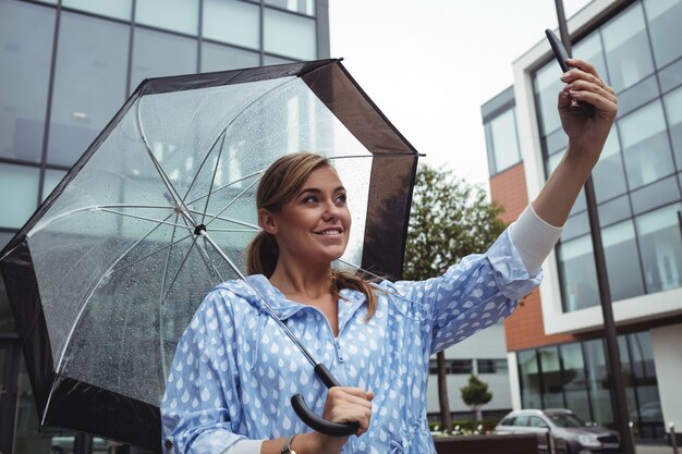 Belle femme avec parapluie en prenant selfie