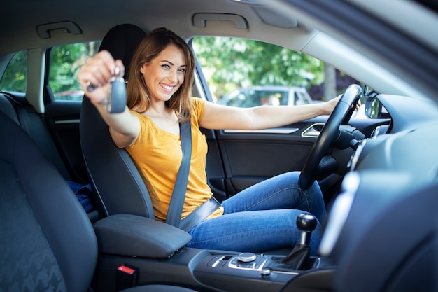Photo gratuite belle femme pilote assis dans son véhicule et tenant des clés de voiture prêtes pour un lecteur