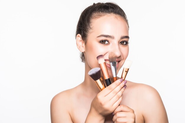 Belle femme avec des pinceaux de maquillage près de son visage isolé sur mur blanc